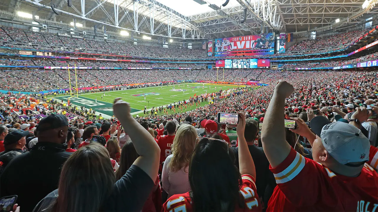 A large crowd of passionate fans cheering in the stadium during the Super Bowl, waving banners and celebrating the game.
