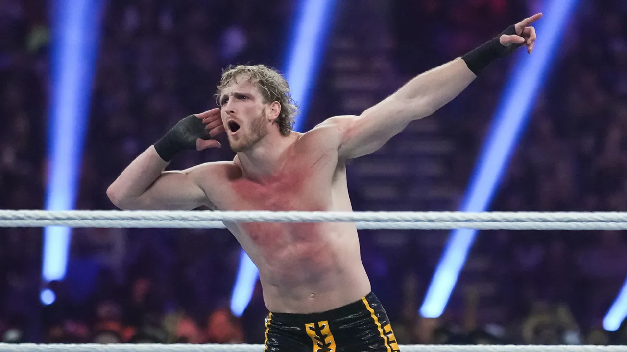 Logan Paul with blond curly hair poses in a WWE ring, engaging with the crowd.