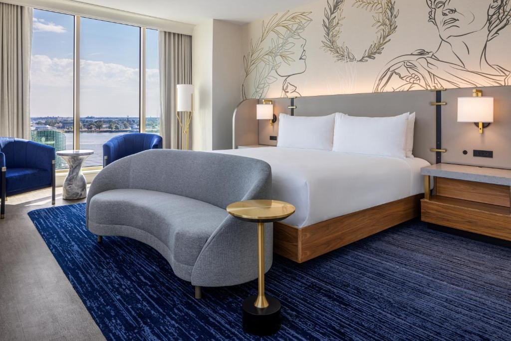 A spacious luxury hotel room with elegant furnishings, large windows showcasing a stunning view of New Orleans.
