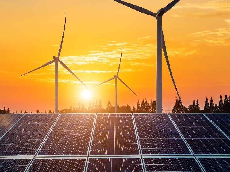 Photograph of wind turbines, solar panels, and green infrastructure in a modern landscape.