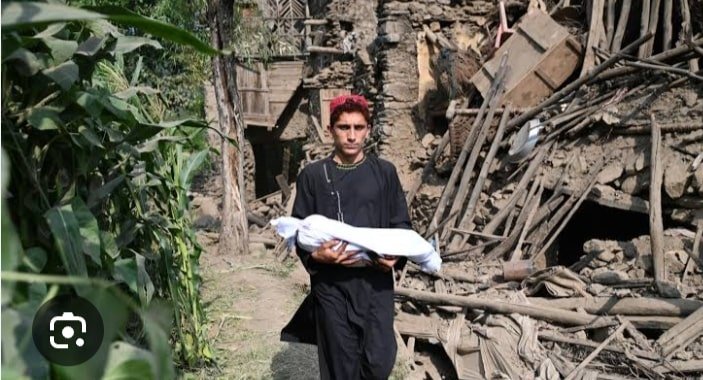 A man carries a child wrapped in a blanket through rubble and damage houses after an Earthquake in Northern Afghanistan